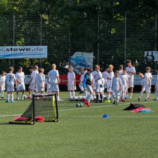 Gruppe von Kindern in weißen Trikots, die auf einem Fußballplatz trainieren.