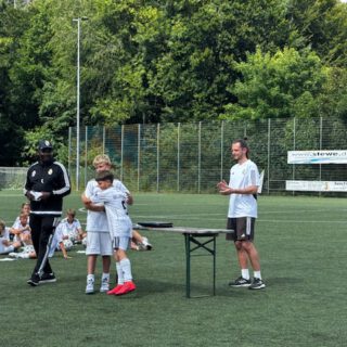 Zwei Kinder umarmen sich nach einer Auszeichnung während eines Fußballtrainings auf einem Sportplatz.