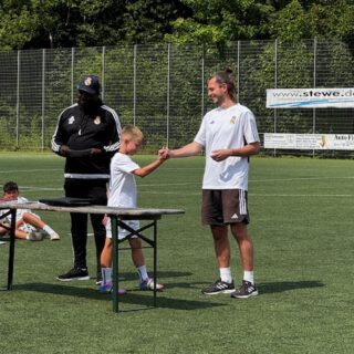 Ein Junge erhält eine Auszeichnung von einem Trainer auf einem Fußballplatz während einer Veranstaltung.