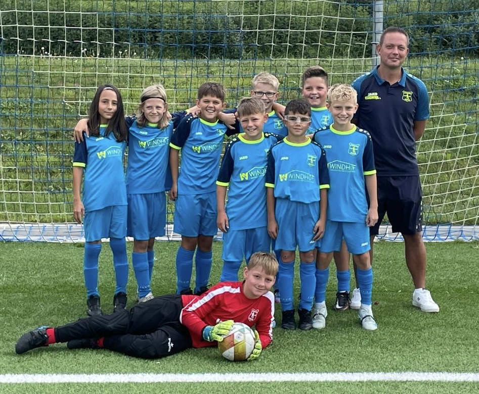 U11 Fußballmannschaft in blauen Trikots mit Trainer auf dem Spielfeld, ein Spieler liegt im Tor.