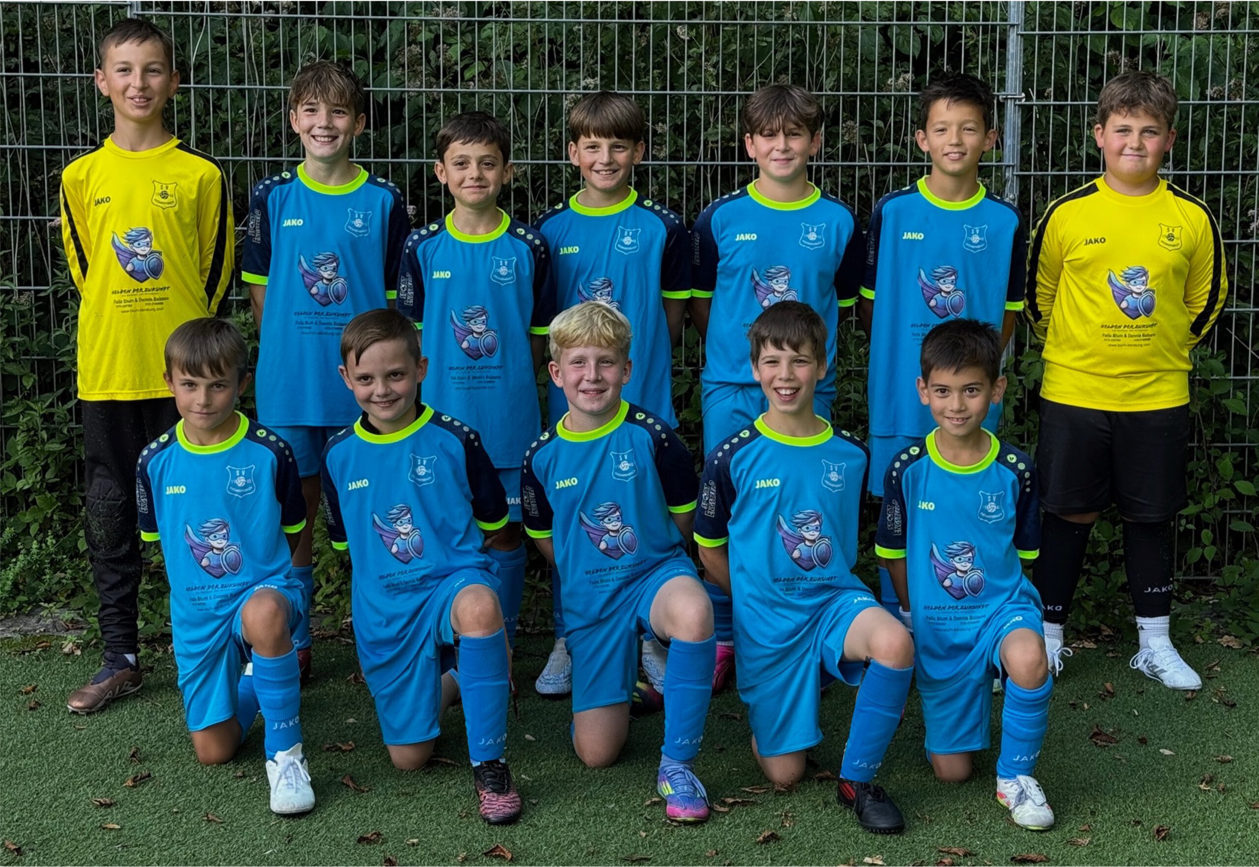 U11 Fußballmannschaft in blauen Trikots mit einem Logo auf der Brust, auf einem Sportplatz aufgestellt.