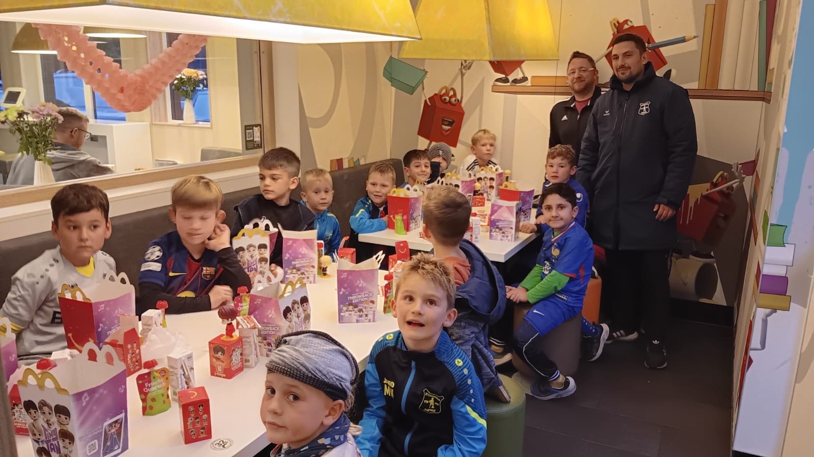 Gruppe von Kindern in einem Restaurant, die an einem Tisch sitzen und feiern, mit Geschenken und Getränken.
