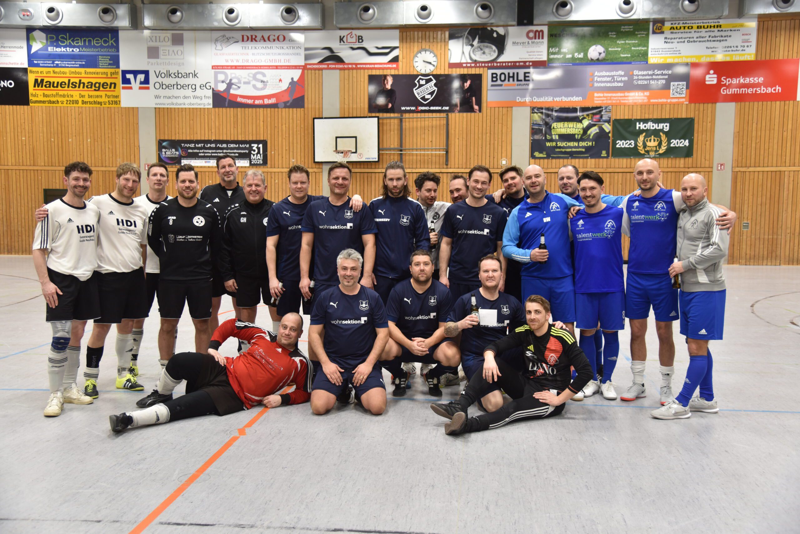 Gruppenfoto von Fu&szlig;ballspielern in blauen und schwarzen Trikots in einer Sporthalle.