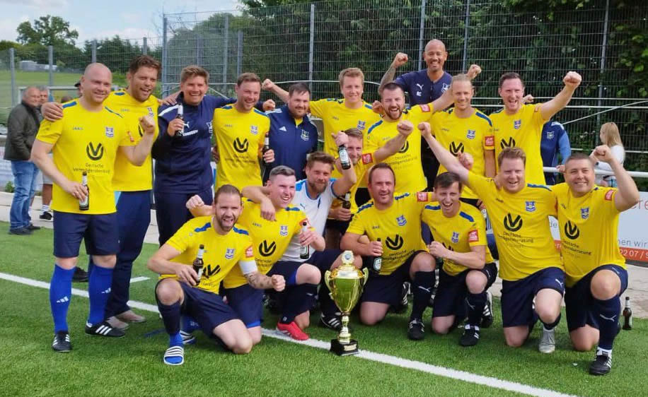 Die Alte Herren Ü32 von SV Frömmersbach jubelt in gelben Trikots auf dem Platz und hält einen großen Pokal nach einem erfolgreichen Spiel hoch.