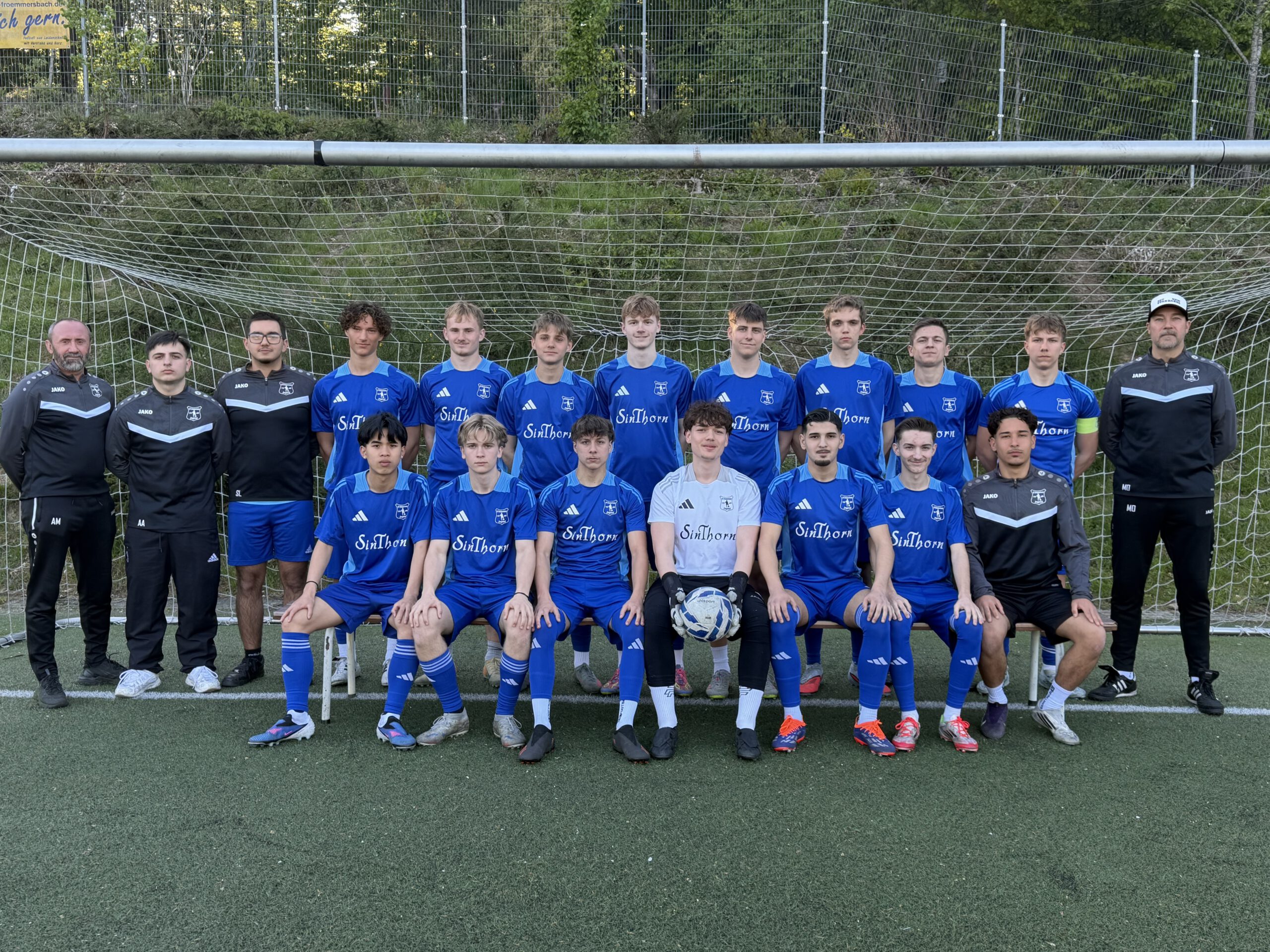 Die U19 A-Junioren von SV Frömmersbach 1948 e.V. posieren in blau-gelben Trikots und Trainingsanzügen vor dem Tor auf dem Sportplatz Am Sonnenberg.