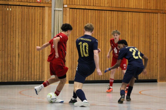 Futsal-Spiel zwischen zwei Teams in einer Sporthalle. Zwei Spieler in roten und blauen Trikots spielen Futsal in einer Sporthalle.