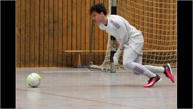 Torwart in Aktion während eines Hallenfußballspiels. Torwart in weißer Ausrüstung springt nach einem Ball während eines Hallenfußballspiels.