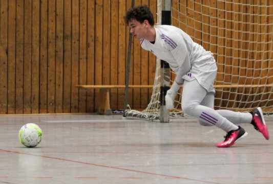 Torwart in Aktion während eines Hallenfußballspiels. Torwart in weißer Ausrüstung springt nach einem Ball während eines Hallenfußballspiels.