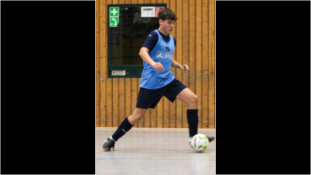 Ein junger Spieler beim Fußballtraining in einer Sporthalle. Junger Fußballspieler in blauer Trainingskleidung, der einen Ball auf einem Hallenfußballfeld spielt.