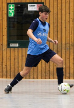 Ein junger Spieler beim Fußballtraining in einer Sporthalle. Junger Fußballspieler in blauer Trainingskleidung, der einen Ball auf einem Hallenfußballfeld spielt.